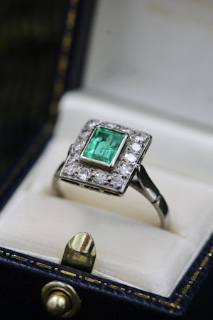 A very fine Platinum (tested) Cluster Ring set with a Modified Step Cut Emerald surrounded by gallery of fourteen Single Cut Diamonds. Circa 1930