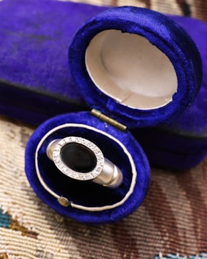 Downstairs at Grays: An 18ct (marked) Brushed White Gold Plaque Ring, with Oval Black Onyx, surrounded by a gallery of Single Cut Diamonds. Circa 1970